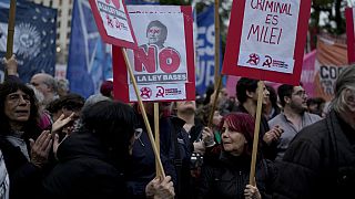 A woman holds a banner, right, that reads in Spanish, "The criminal is Milei"during a demonstration at the Plaza de Mayo demanding the release of those detained in a protest.