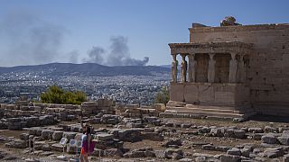 A woman poses for a photo in front Caryatid statues that prop up the porch of the 5th century B.C. Erechtheion temple in Athens.