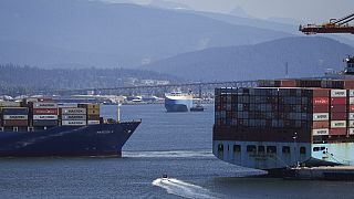 FILE - A boater passes between cargo ships on the harbour, in Vancouver, British Columbia, July 16, 2024. (Darryl Dyck/The Canadian Press via AP, File)
