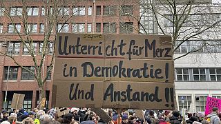 People gather to protest against the Far Right, in Cologne, Germany, Saturday Jan. 25, 2025. Banner reads: "Immediate lessons for Merz in democracy and decency". (Christoph Dr