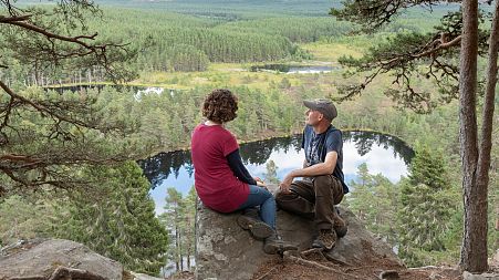 A couple sit and look out across Uath Lochans in Cairngorms National Park, Scotland 