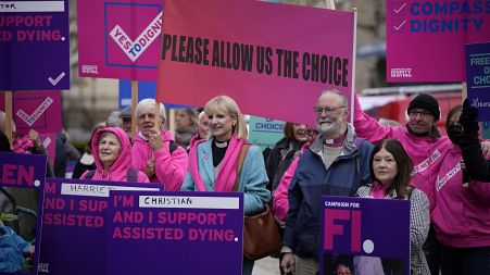 Campaigners holds signs as they rally for assisted dying access in October 2021 outside the Houses of Parliament in London. 