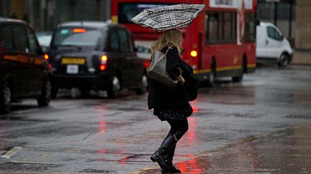 A woman's umbrella is blown inside out as she walks through a heavy rain shower in the Canary Wharf business district of London, Wednesday, Nov. 20, 2013.