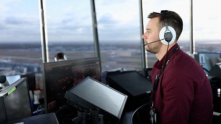 Air traffic controller in the tower's top floor control room overlooking the Heathrow Airport runways and airfield, and giving instructions to pilots