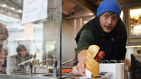 A vendor serves a hot dog at a traditional sausage stand 